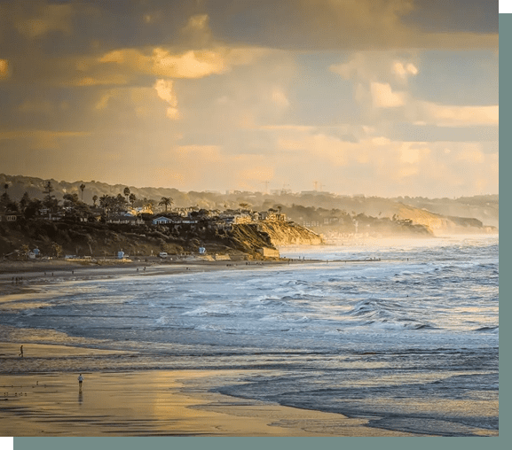 A serene beach at sunset with waves gently crashing and a cloudy sky.