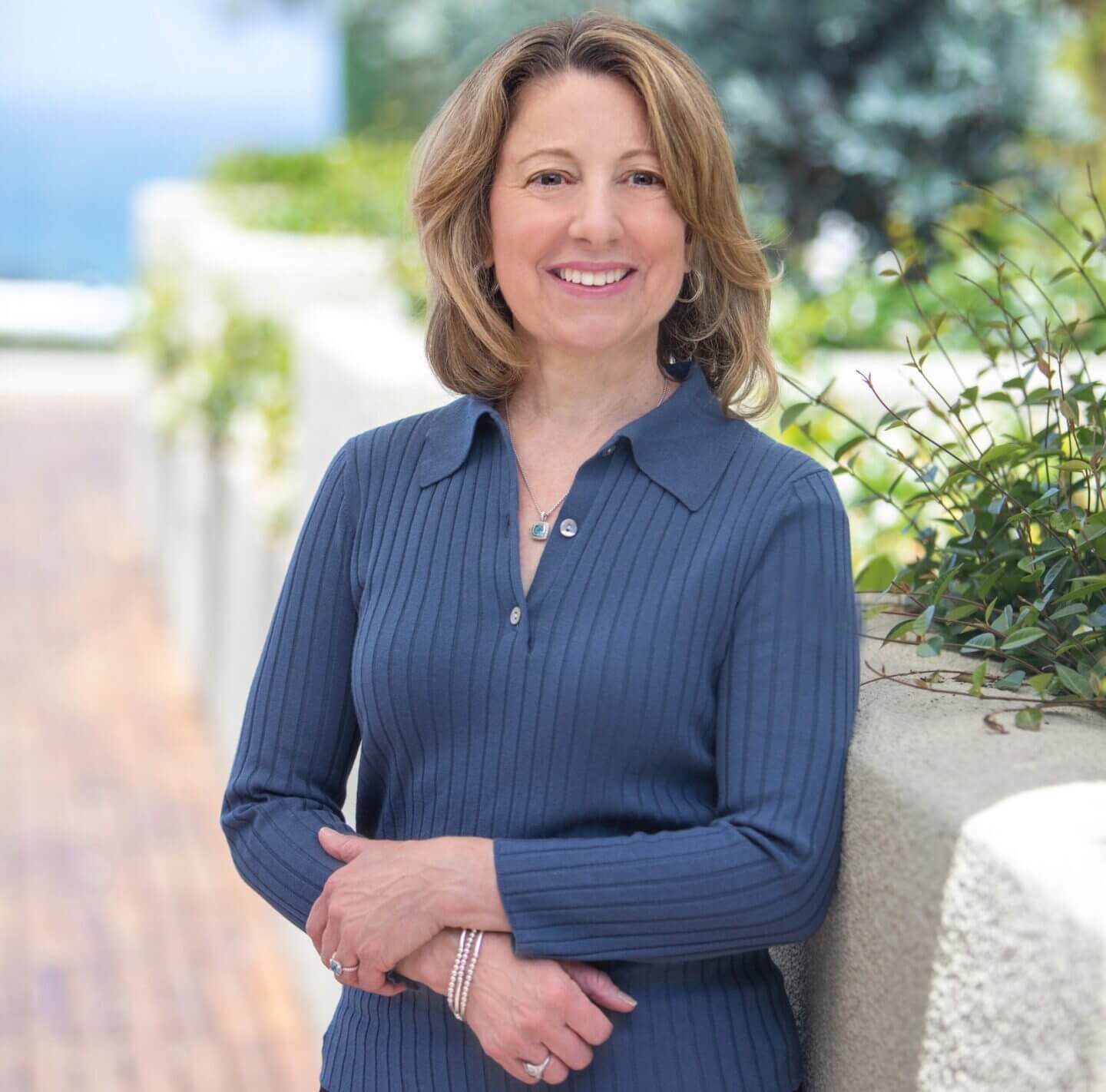 Smiling woman in blue sweater, outdoor setting.